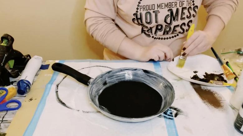 A woman paints an old frying pan with black and white paint.