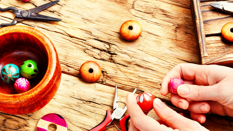 Hands hold large wooden beads above a wooden tabletop covered in more beads and tools.