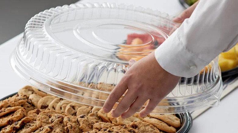 Woman lifts plastic platter lid from a tray of cookies.