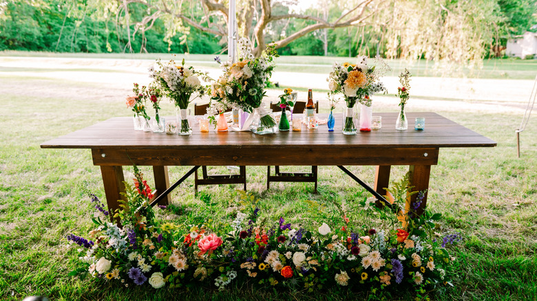 Mason jars filled with flowers are the centerpieces on an outdoor table.