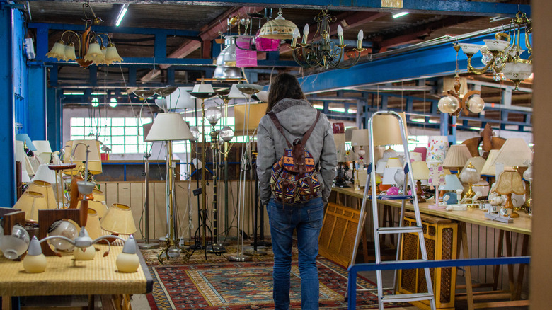 A woman walks through an aisle of various lamps at a thrift store