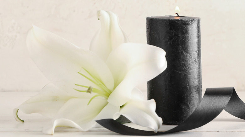 A black candle and ribbon with a white flower