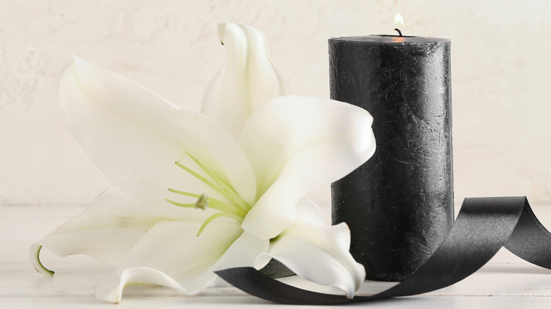 A black candle and ribbon with a white flower