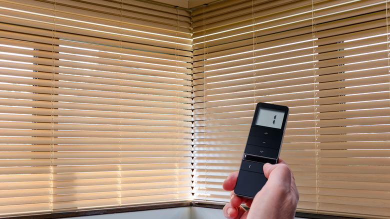 Hand holding remote control used to operate window blinds on a corner window.