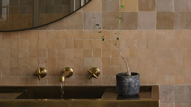 A tan zellige tile backsplash behind a bathroom sink and mirror