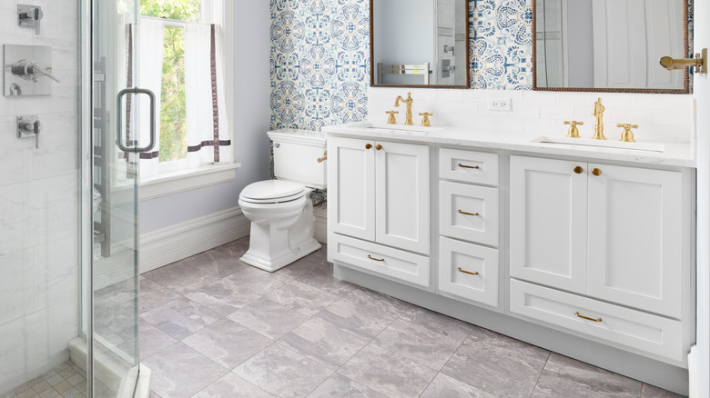 A modern bathroom with blue and white pattern wallpaper, white cabinets, and natural sunlight.