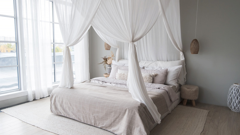 A beautiful bright bedroom featuring light linens and a sheer white bed canopy.