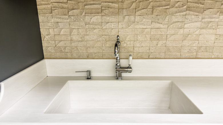 A sink with an unglazed stone tile backsplash.