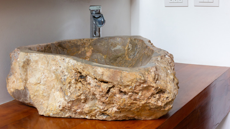 A raw stone wink basin on a wood countertop.