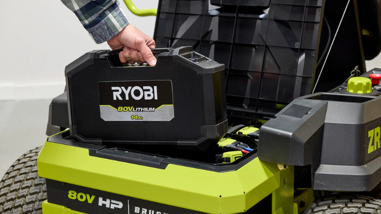 A person putting Ryobi's new 18V 14Ah Lithium Battery into their lawn mower