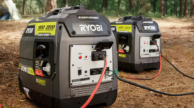 Two of Ryobi's 2500 Watt Gas Inverter Generators sit on dirt at a campsite with cords plugged into them