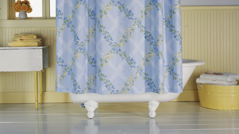 a clawfoot bathtub and a blue floral shower curtain that doesn't quite meet the floor