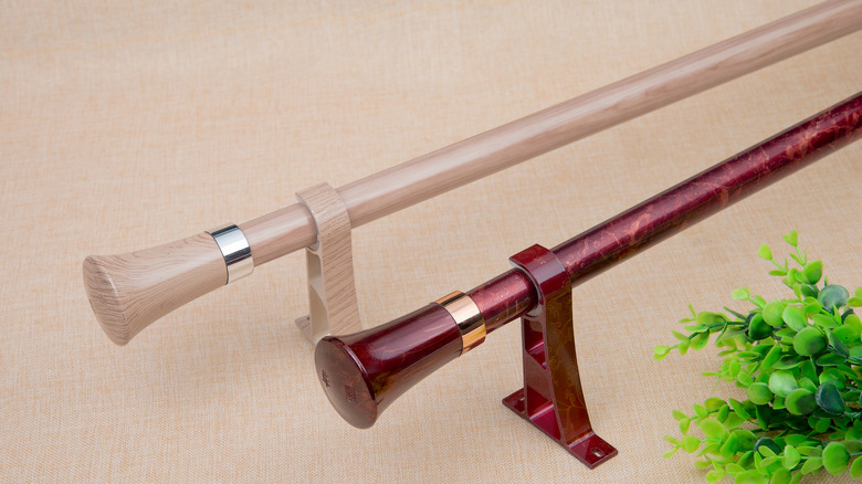 Two curtain rails rest on a fabric surface by a plant.