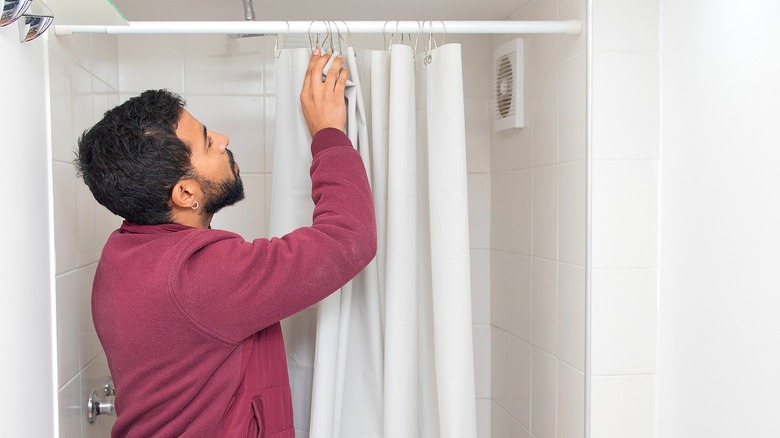 A person in a red sweater inspecting the hooks on a shower curtain in a bathroom.