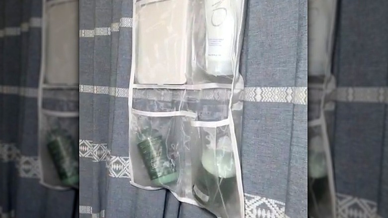 The Misslo white mesh shower organizer filled with bottles of soap hanging over a grey shower curtain