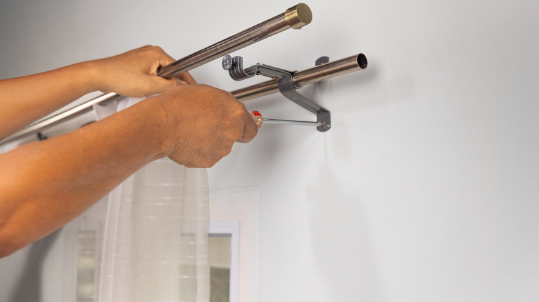 Hands hang curtain rod.