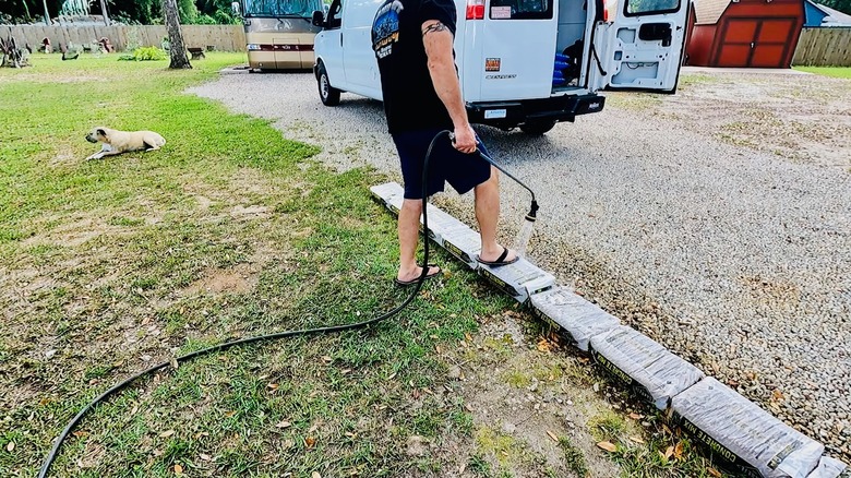DIYer sprays concrete bags with water while tamping bags with his foot.
