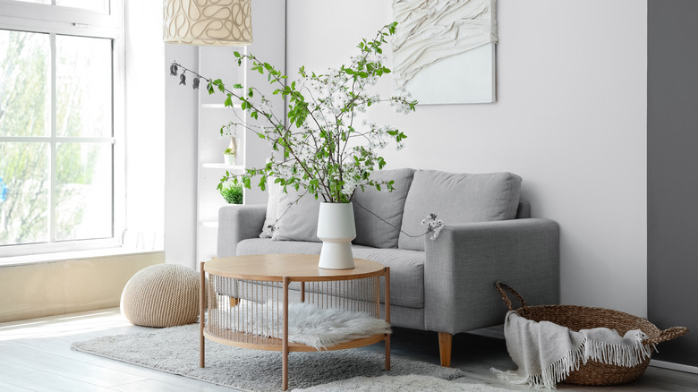 Comfortable sofa and vase with blooming branches on coffee table in living room