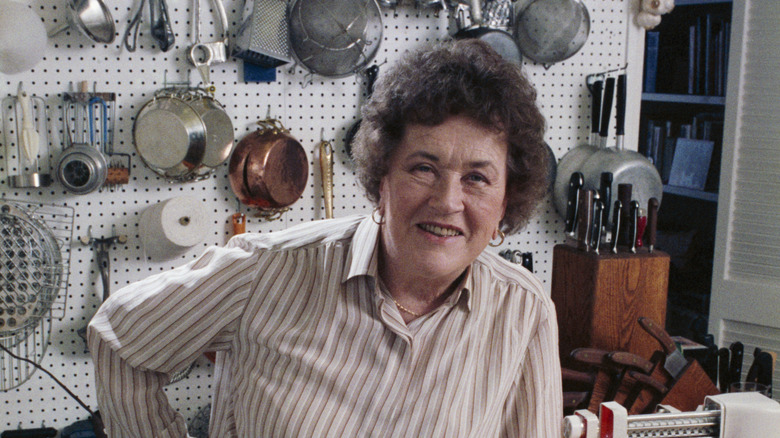 Julia Child in her kitchen with pots and utensils hanging in the background.
