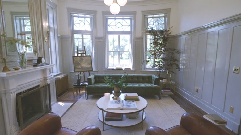 Living room with a green sofa, red leather chairs, and a fireplace that has high wainscoting painted gray on one wall.