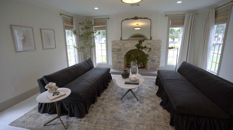 Living room with two dark gray skirted sofas separated by a marble coffee table and a fireplace on the far end.