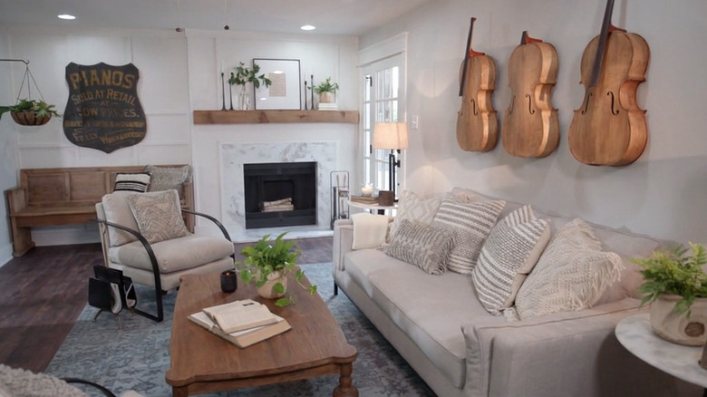 A living space with a white sofa that features three cellos hanging on one wall and a vintage piano sign on another wall.