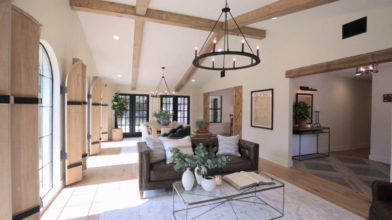 An open concept living room backing onto a dining room that features wooden beams on ceiling and wooden doors that are used as window coverings.