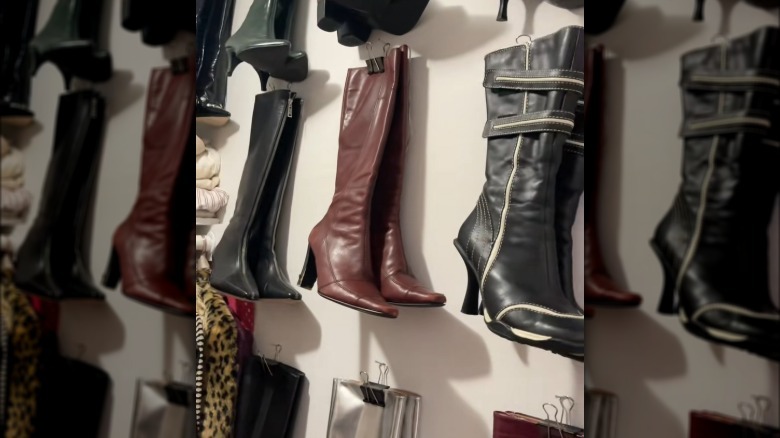 Tall-shaft boots hanging from binder clips attached to a wall.