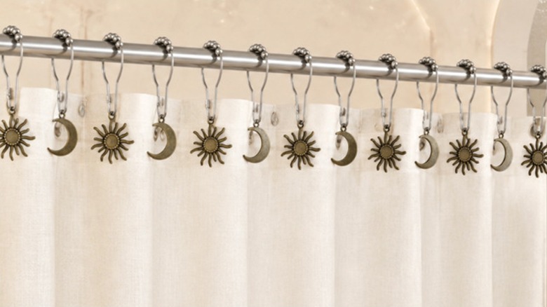 The sun and moon shower curtain charms hanging from a white shower curtain
