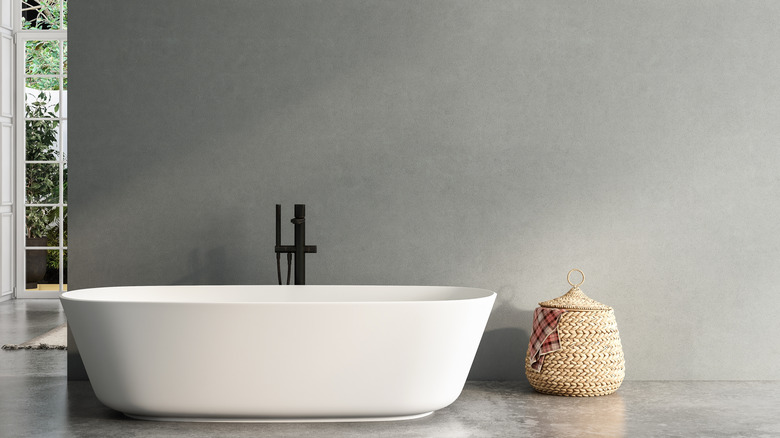 A white soaking tub placed against a gray wall.