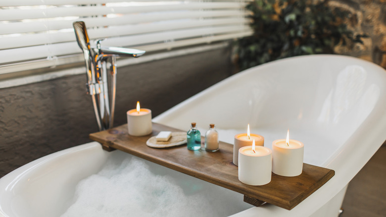 A bathtub next to a window with candles and essential oils.