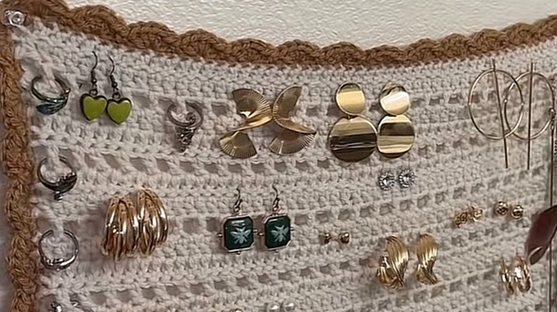 A close up of crochet blanket with earrings hanging on it or pinned to it.