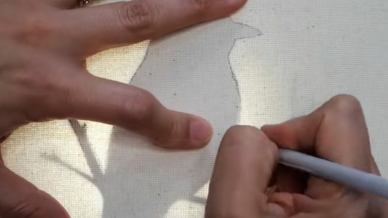 A pair of light-skinned hands trace a bird outline on a canvas.
