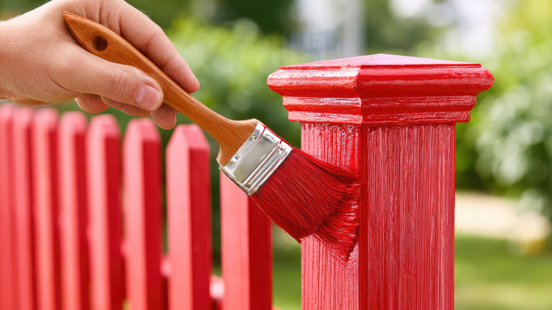 someone painting a fence post in red paint