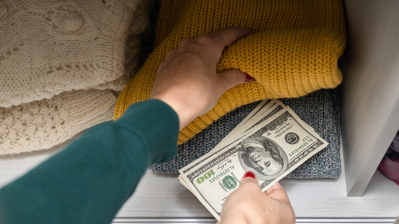 A person hiding some dollar notes in between folded clothes in a closet