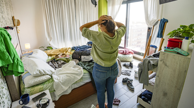 A person with hands on head in a messy room