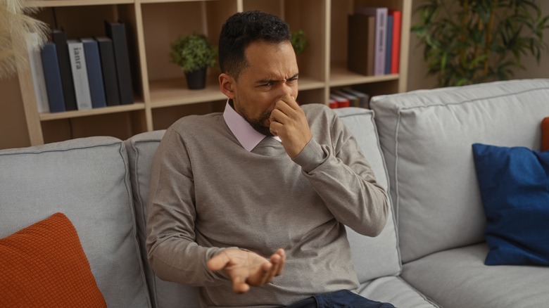 Man covering nose while sitting on smelly couch
