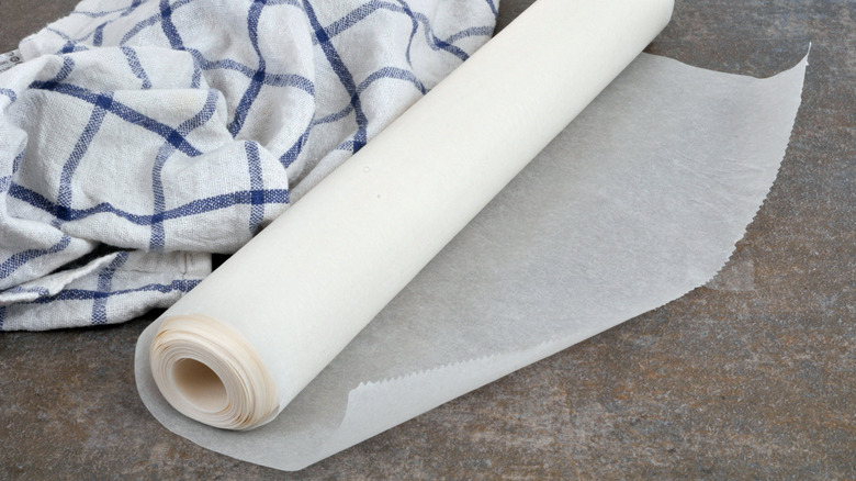 A roll of wax paper on a surface next to a dish cloth