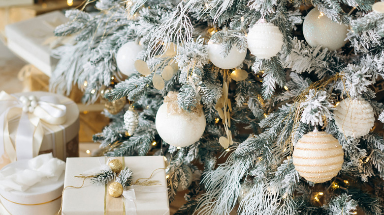 A frosted Christmas tree with frost, decorative white ornaments, and presents