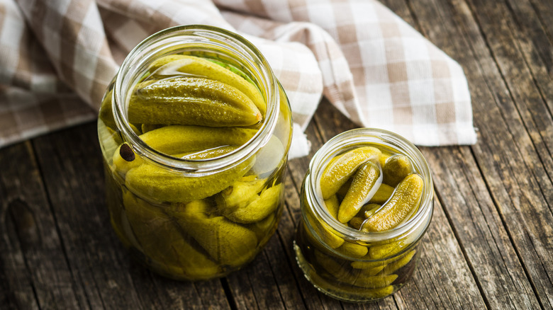 Two different sized pickle jars filled with pickles on a wood table with a checkered hand towel