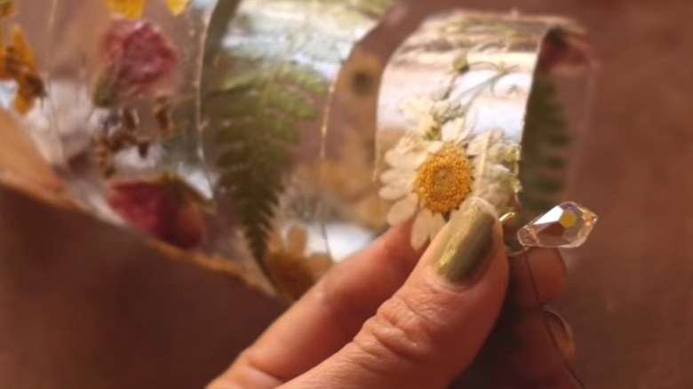 Thumb holding a crystal bead onto a DIY spiral flower suncatcher project.