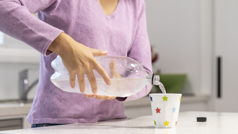 A person pouring clear soda from a plastic bottle.