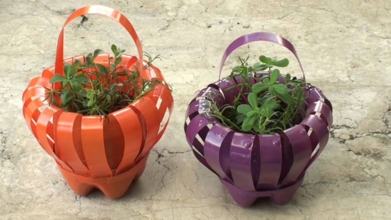 Flower baskets made from plastic water bottles, painted orange and purple, hold small bunches of greenery.