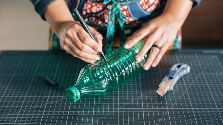 Someone drawing on a plastic water bottle before cutting it