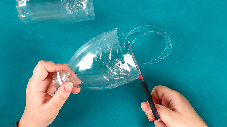 Hands cut an empty plastic water bottle in half with scissors.