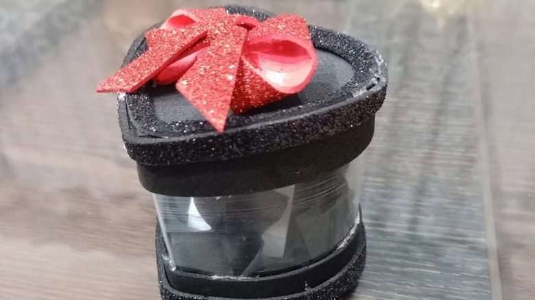 A glittery black heart-shaped trinket box made from a plastic bottle with a red glitter bow on top of the lid.