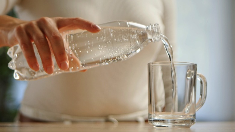 woman pouring water into cup from clear plastic water bottle