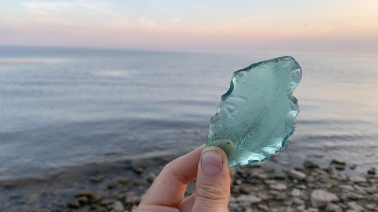 A hand holds up a blue, ruffled piece of glass against a beach background
