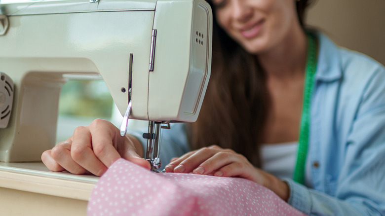 A person sews a pink, patterned fabric using a sewing machine
