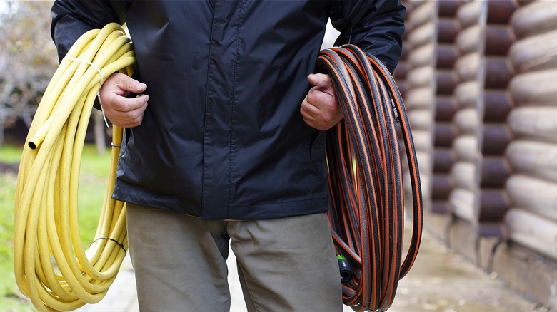 Man holding two coiled up garden hoses